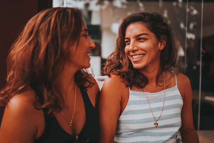 Twee jonge vrouwen in gesprek met elkaar, warm avondlicht.