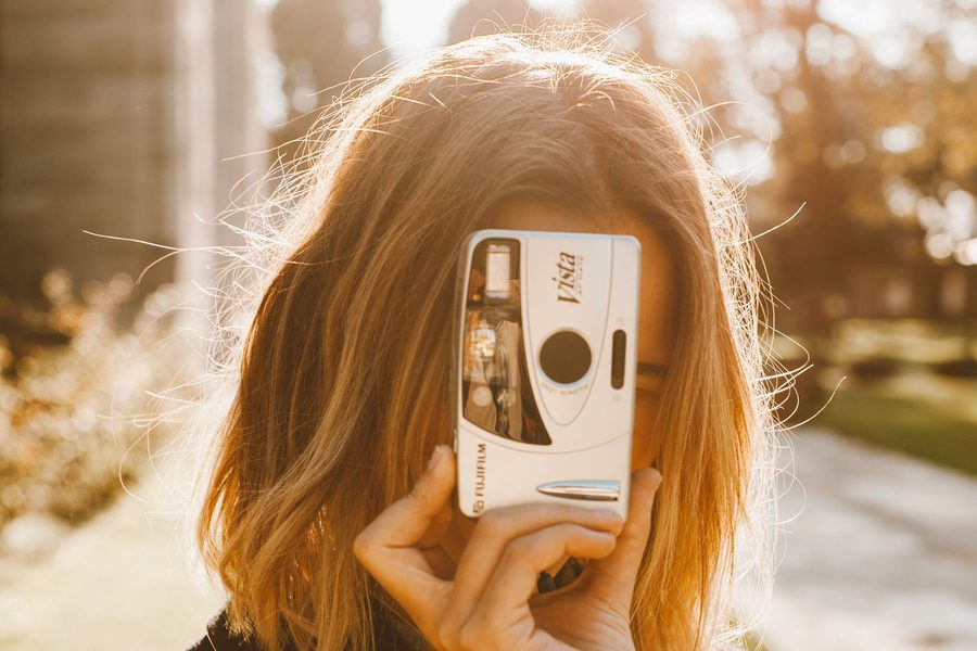 Jonge vrouw houdt een camera voor haar gezicht, tegenlicht.